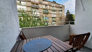 A balcony with a wooden table and chairs, a blue mat, and a view of a multi-story building. - Apartment Freyja (Split)
