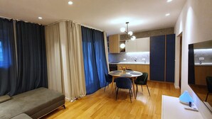 A modern living room with a sofa, a dining table with chairs, and a kitchen area with cabinets and a sink. - Apartment Freyja (Split)