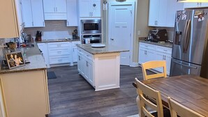 A modern kitchen with white cabinets, a wooden dining table, and a patterned rug. - Cheerful 2 bed 1 bath w/patio. 10 min from beach,  dog friendly! (Navarre)