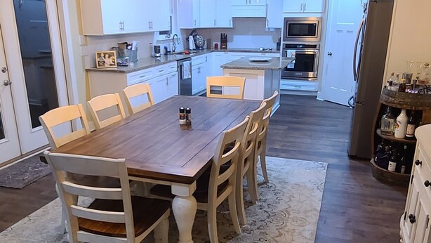 A spacious kitchen with a dining area, featuring wooden flooring, white cabinetry, and pendant lighting. - Cheerful 2 bed 1 bath w/patio. 10 min from beach,  dog friendly! (Navarre)