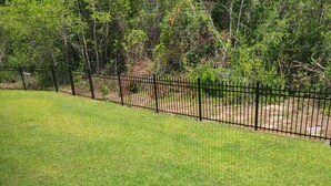 A grassy yard with a black metal fence and trees in the background. - Cheerful 2 bed 1 bath w/patio. 10 min from beach,  dog friendly! (Navarre)