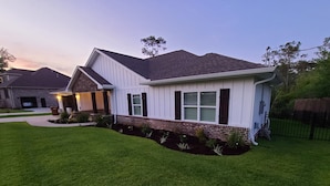 A single-story house with a brick foundation and white siding, a front porch, and a well-maintained lawn. - Cheerful 2 bed 1 bath w/patio. 10 min from beach,  dog friendly! (Navarre)