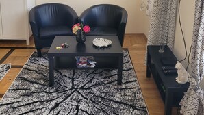 Ett vardagsrum med en svart lädersoffa, ett soffbord med blommor och en tv som står på ett tv-bord.