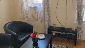 Ett vardagsrum med en svart lädersoffa, ett soffbord med en vas med blommor, en platt-TV som är monterad på väggen och en mönstrad matta.