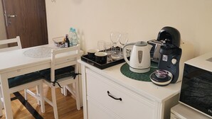 Ett litet, praktiskt kök med en kaffebryggare, vattenkokare och mikrovågsugn. Här finns ett matbord med stolar och ett litet skåp med lådor.