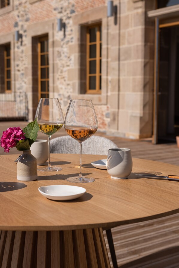 A round wooden table with two wine glasses, a white vase with pink flowers, and a white pitcher. - Cueillette (Altillac)