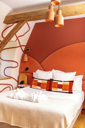 A bedroom with a large bed, a wooden ceiling beam, and a modern pendant light. - Cueillette (Altillac)