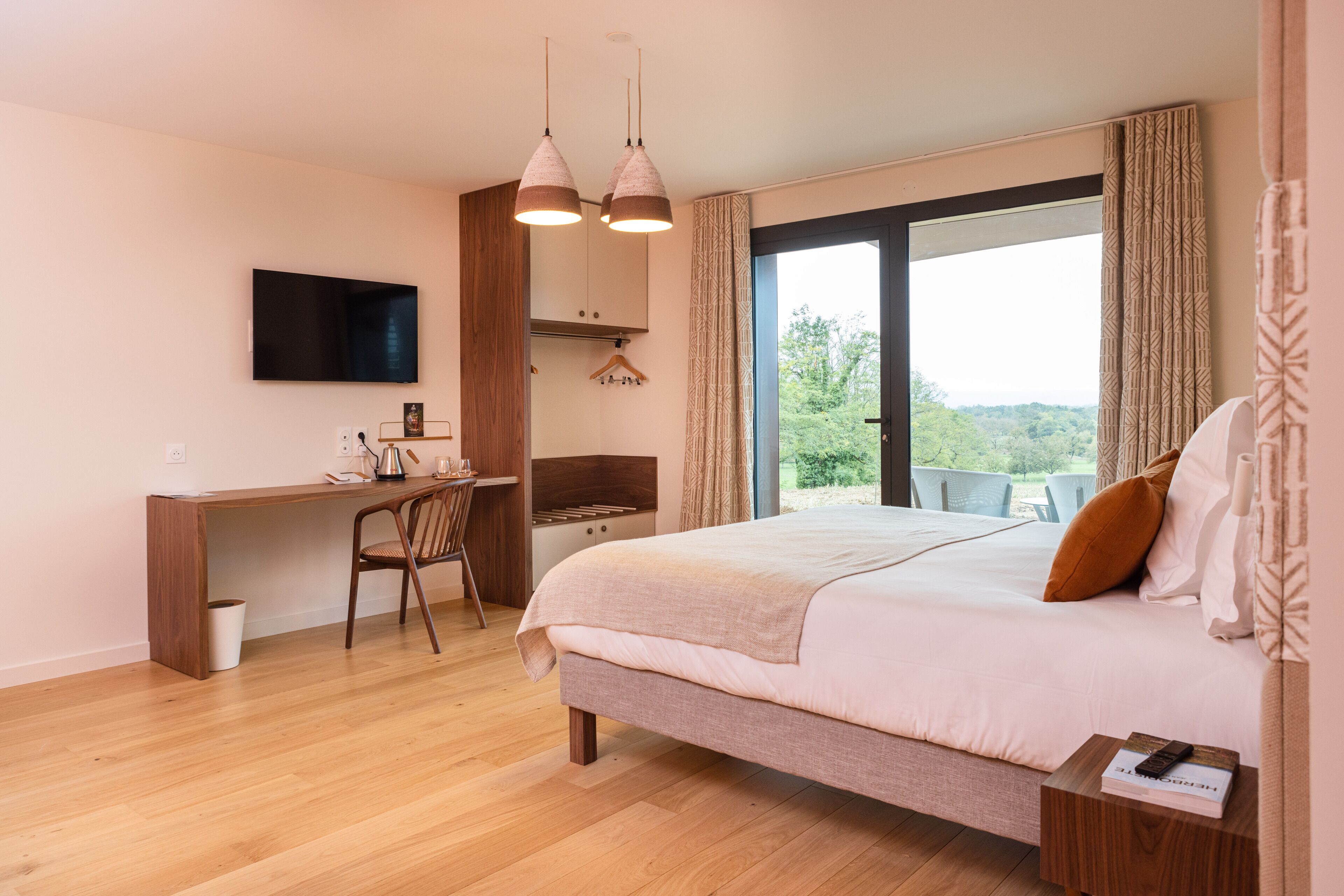 A bedroom with a bed, a desk, a chair, a TV, and a balcony with a view.