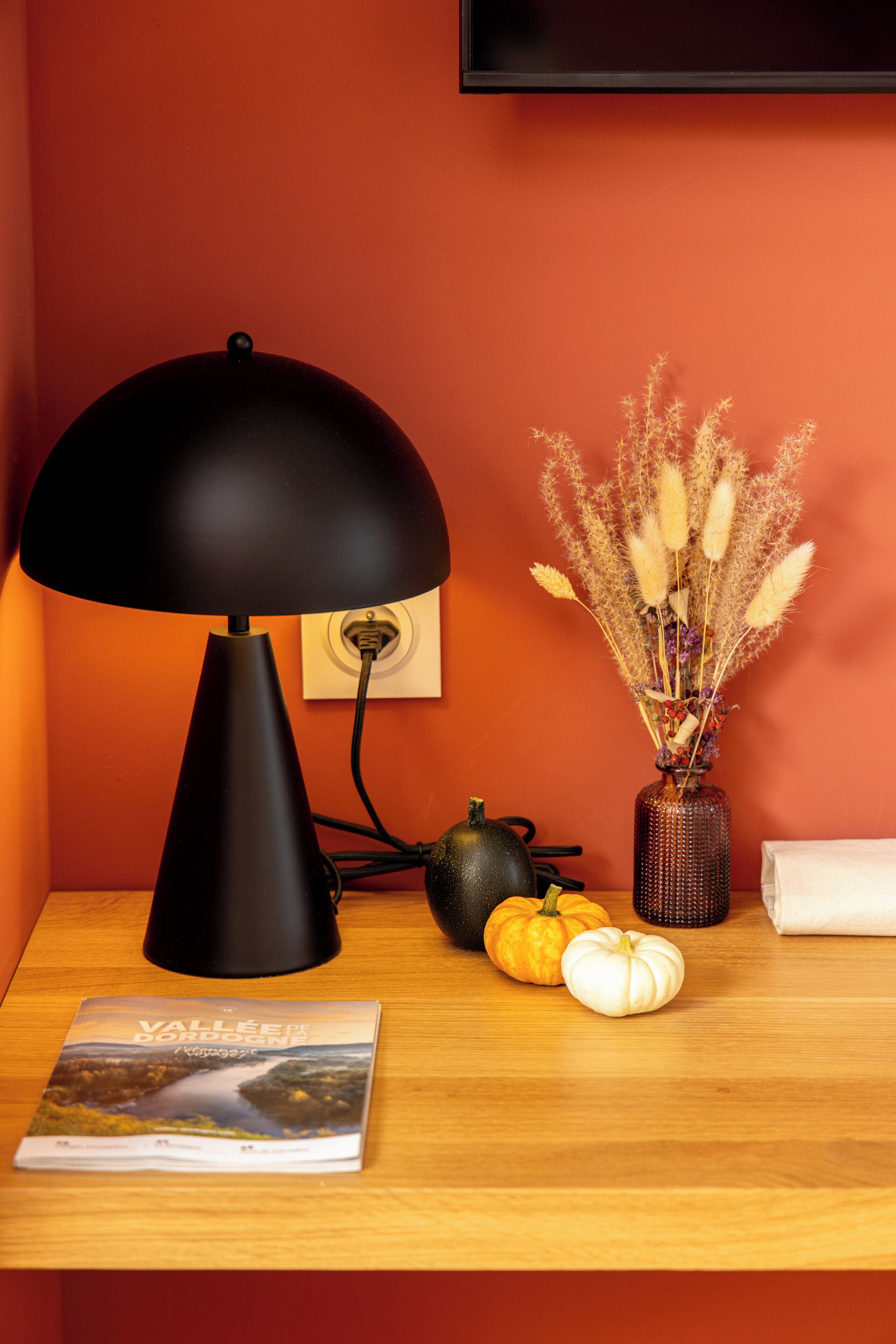 A desk with a black lamp, a vase with dried plants, two pumpkins, and a book titled "Valle de los Santos."