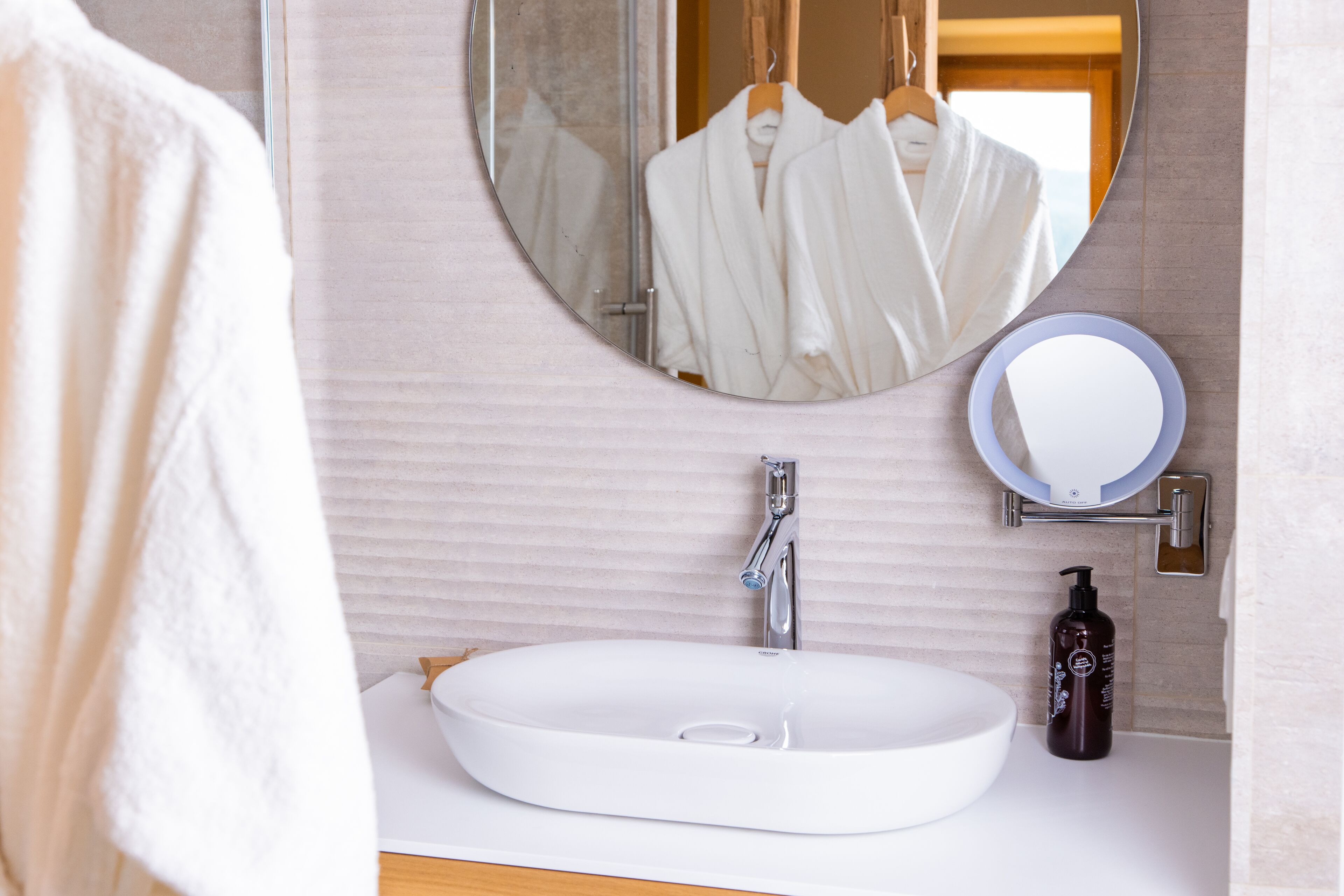 A bathroom with a white sink, a round mirror, and a bottle of shampoo.