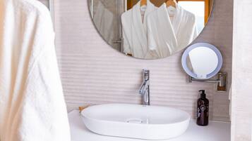 A bathroom with a white sink, a round mirror, and a bottle of shampoo.