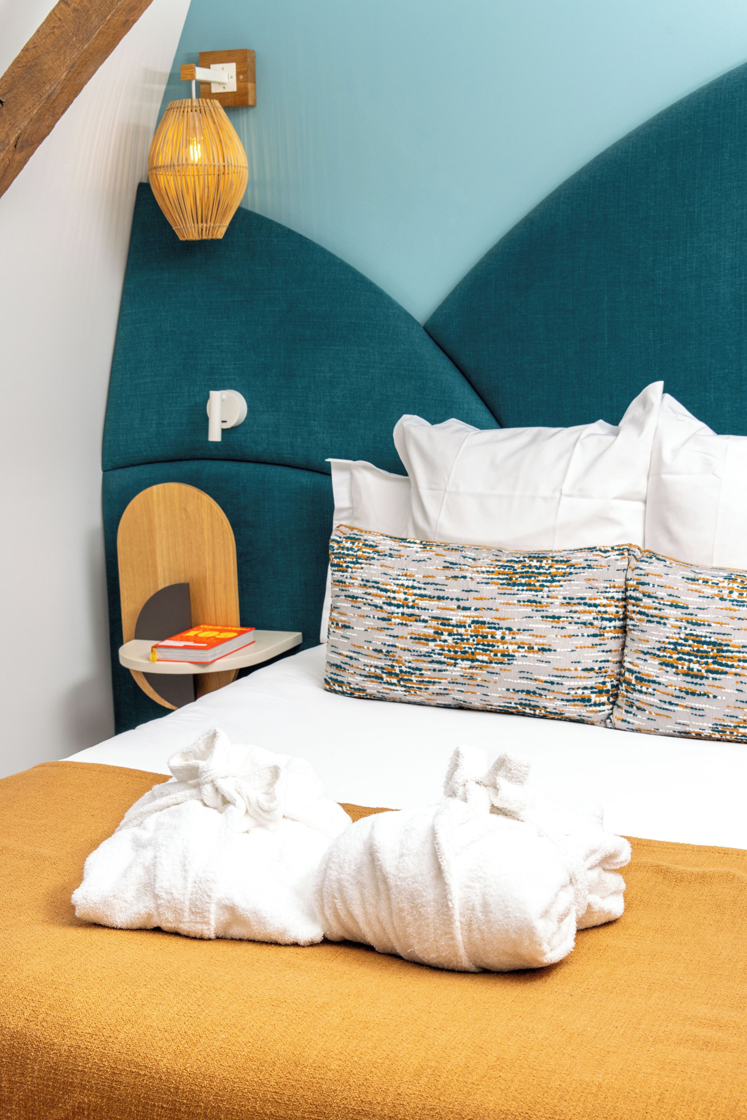 A neatly made bed with white linens, a teal headboard, and a patterned pillow.