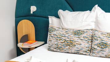 A neatly made bed with white linens, a teal headboard, and a patterned pillow.