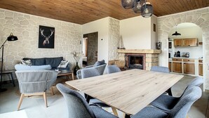 Ein geräumiger Wohnbereich mit Steinwand, Kamin, Holzbalkendecke und Esstisch mit Stühlen.