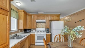 A kitchen with wooden cabinets, a stove, a refrigerator, a microwave, and a dining table with chairs. - *Cottage #3 @ Fisherman's Landing (boat shelter)* (Langston)