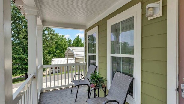 A covered porch with two chairs and a potted plant, a white railing, and a green wall. - *Cottage #3 @ Fisherman's Landing (boat shelter)* (Langston)