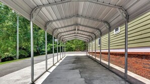 A covered walkway with metal railings, a brick wall on one side, and a green building in the background. - *Cottage #3 @ Fisherman's Landing (boat shelter)* (Langston)