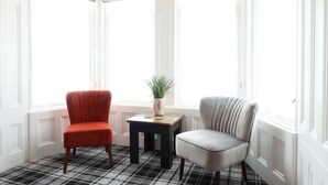 A room with a checkered floor, two chairs, a small table with a plant, and large windows with patterned curtains. - The Craft House (Plymouth)