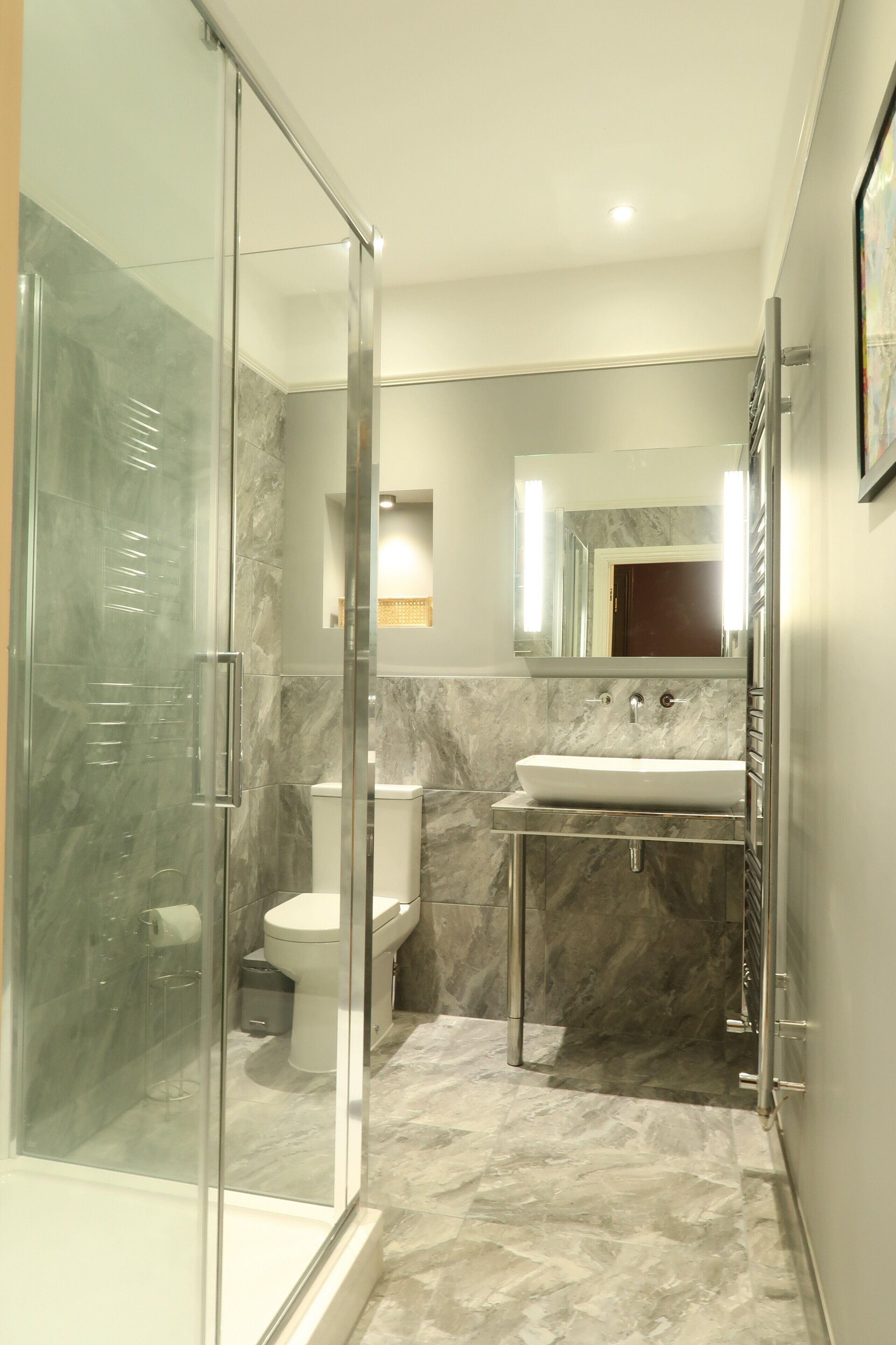 Une salle de bain moderne avec une douche en verre, un lavabo blanc et un sol carrelé en marbre.