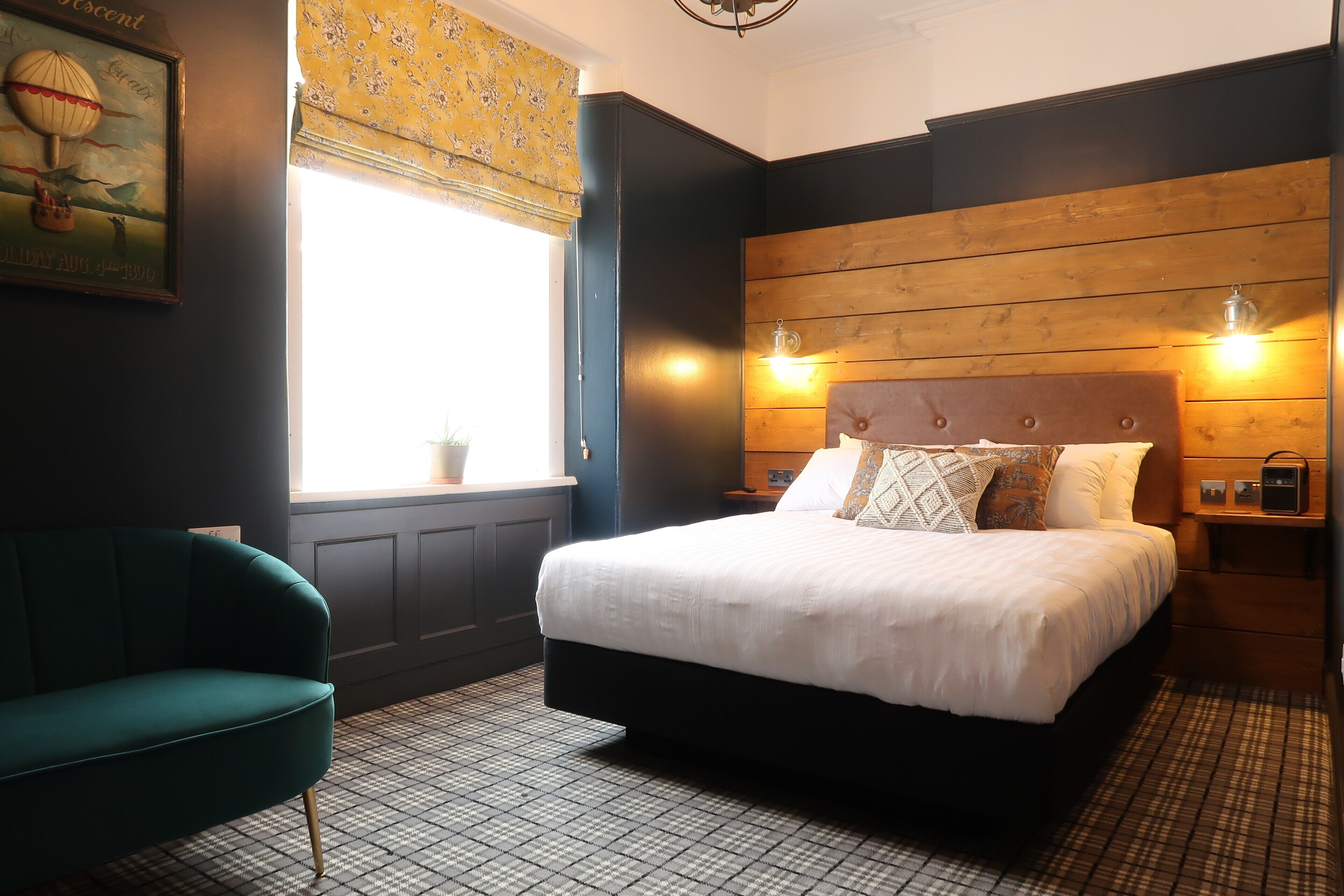 A bedroom with a large bed, a green armchair, a wooden headboard, and a window with a view of the sky.