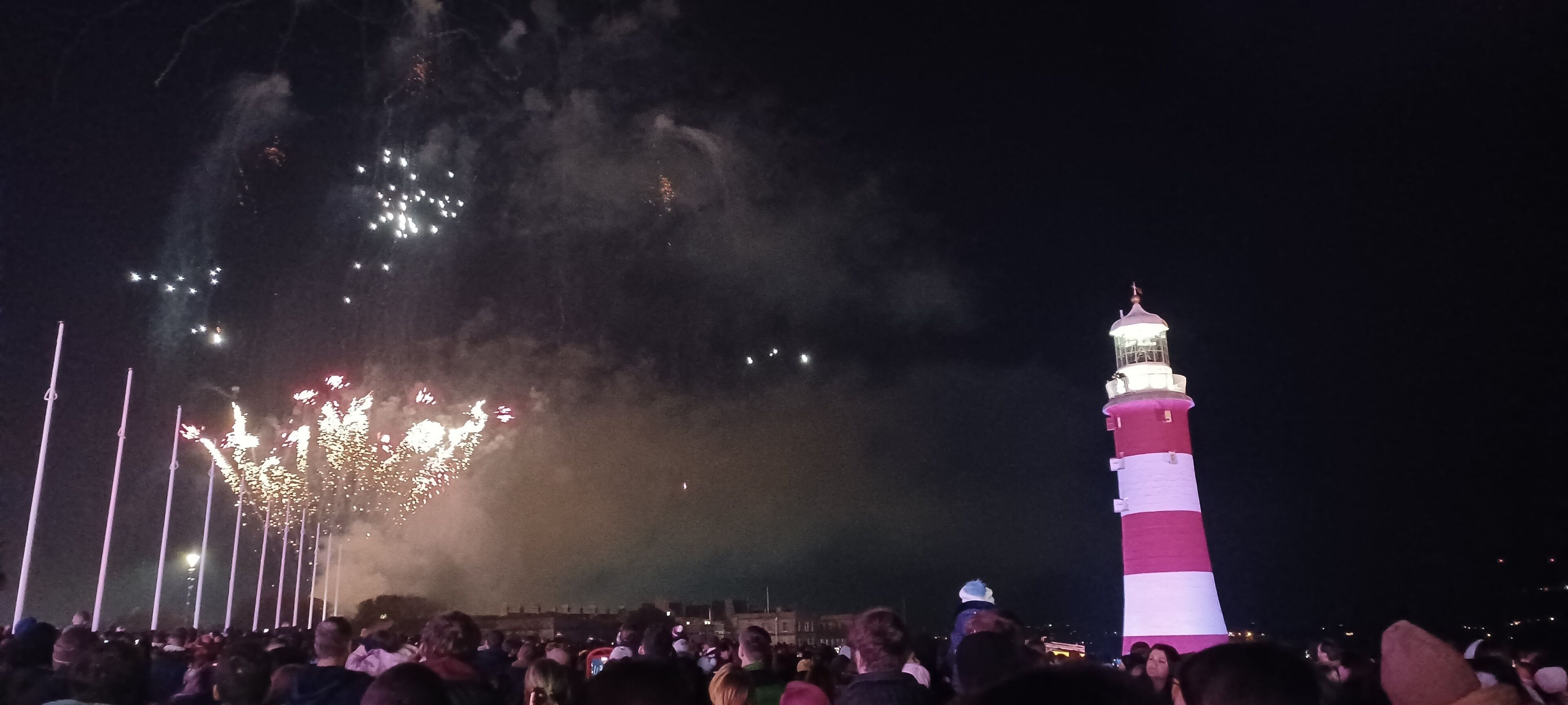 A lighthouse at night with a crowd of people in the foreground.