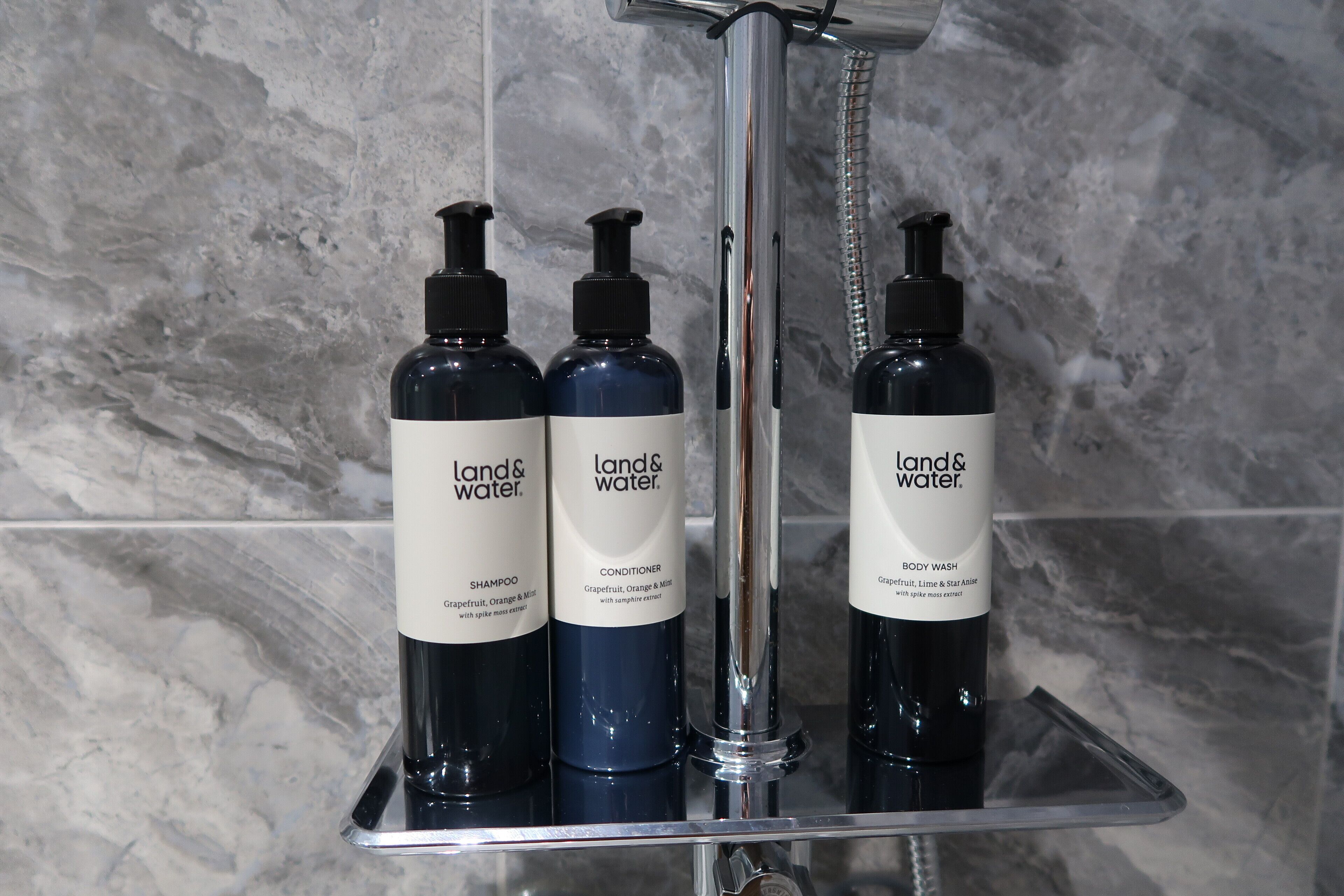 Tres botellas de productos Land & Water sobre un estante en el baño.