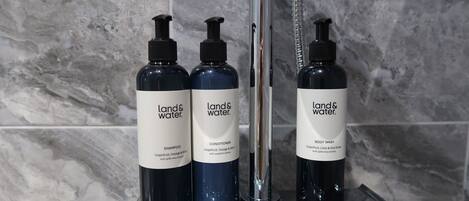 Tres botellas de productos Land & Water sobre un estante en el baño.