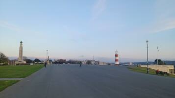 A wide, open paved area with a monument and a lighthouse in the distance.