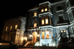 A multi-story building with illuminated windows and a grand entrance. - The Craft House (Plymouth)