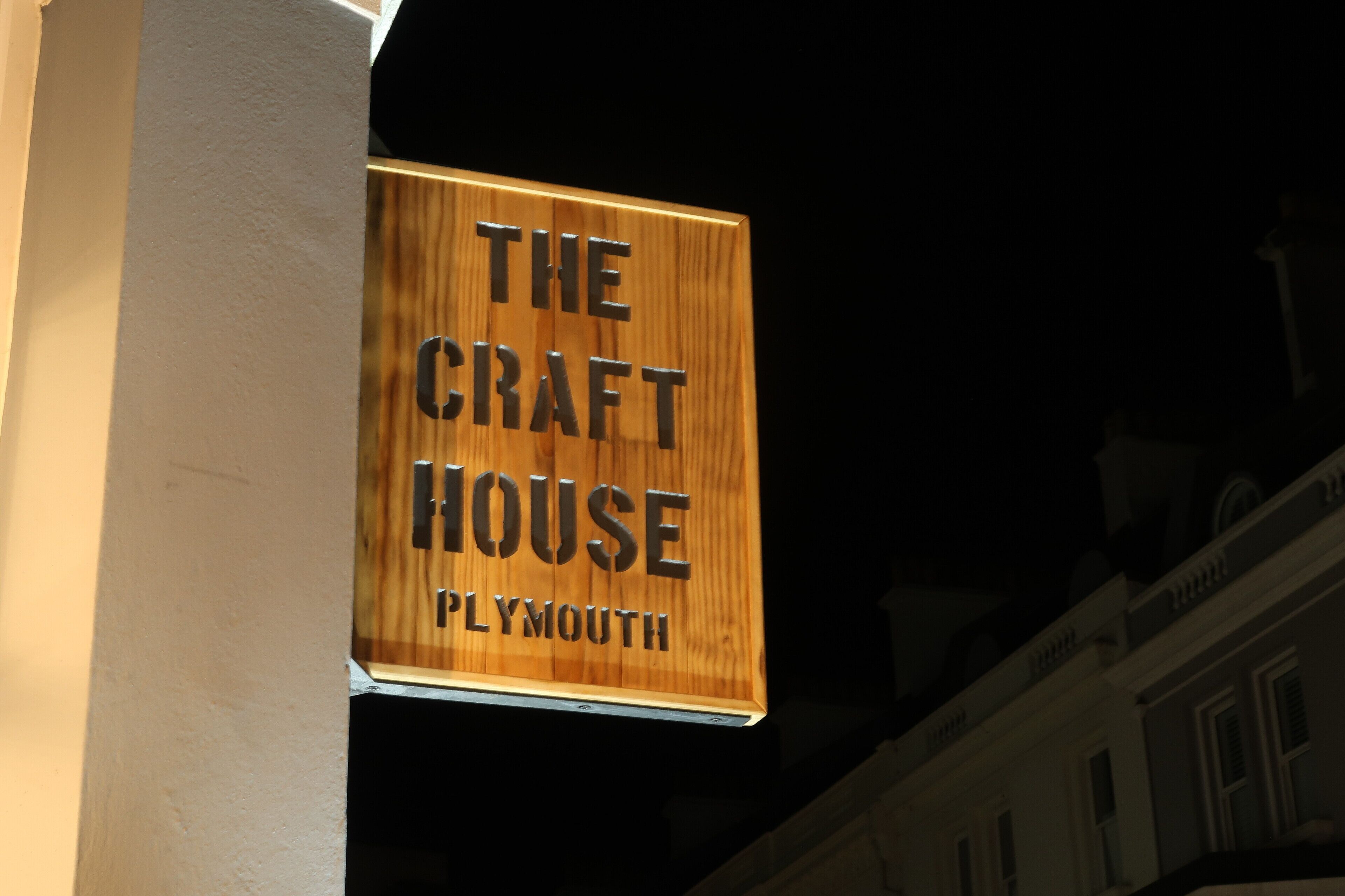 A wooden sign with the text "THE CRAFT HOUSE" and "PLYMOUTH" against a dark background.