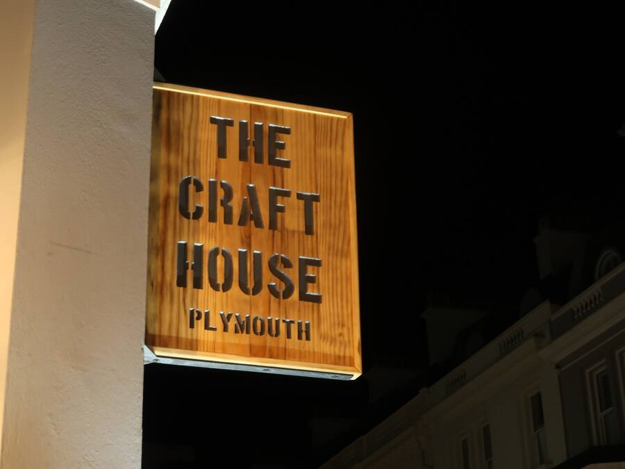 Un cartell de fusta amb el text "THE CRAFT HOUSE" i "PLYMOUTH" sobre un fons fosc.