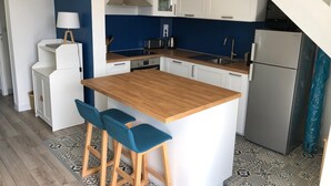 A compact kitchen with a wooden island, white cabinets, and a stainless steel refrigerator.