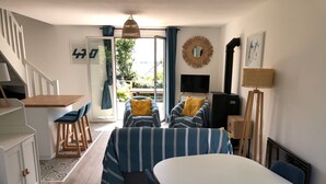 A cozy room with a bed, a desk, and a TV. There is a window with curtains, a wall clock, and a door.