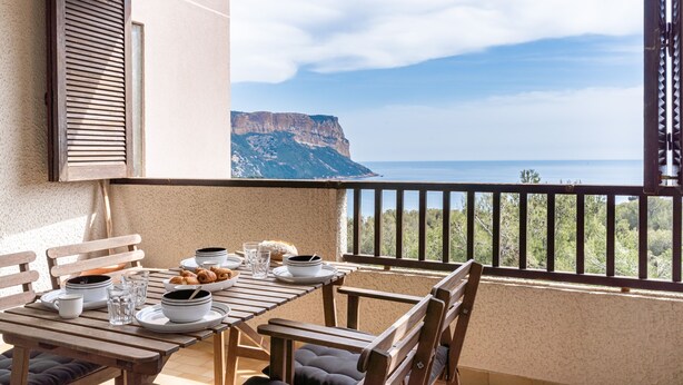 Un balcón con una mesa dispuesta para el desayuno, con vista a un acantilado y al mar.