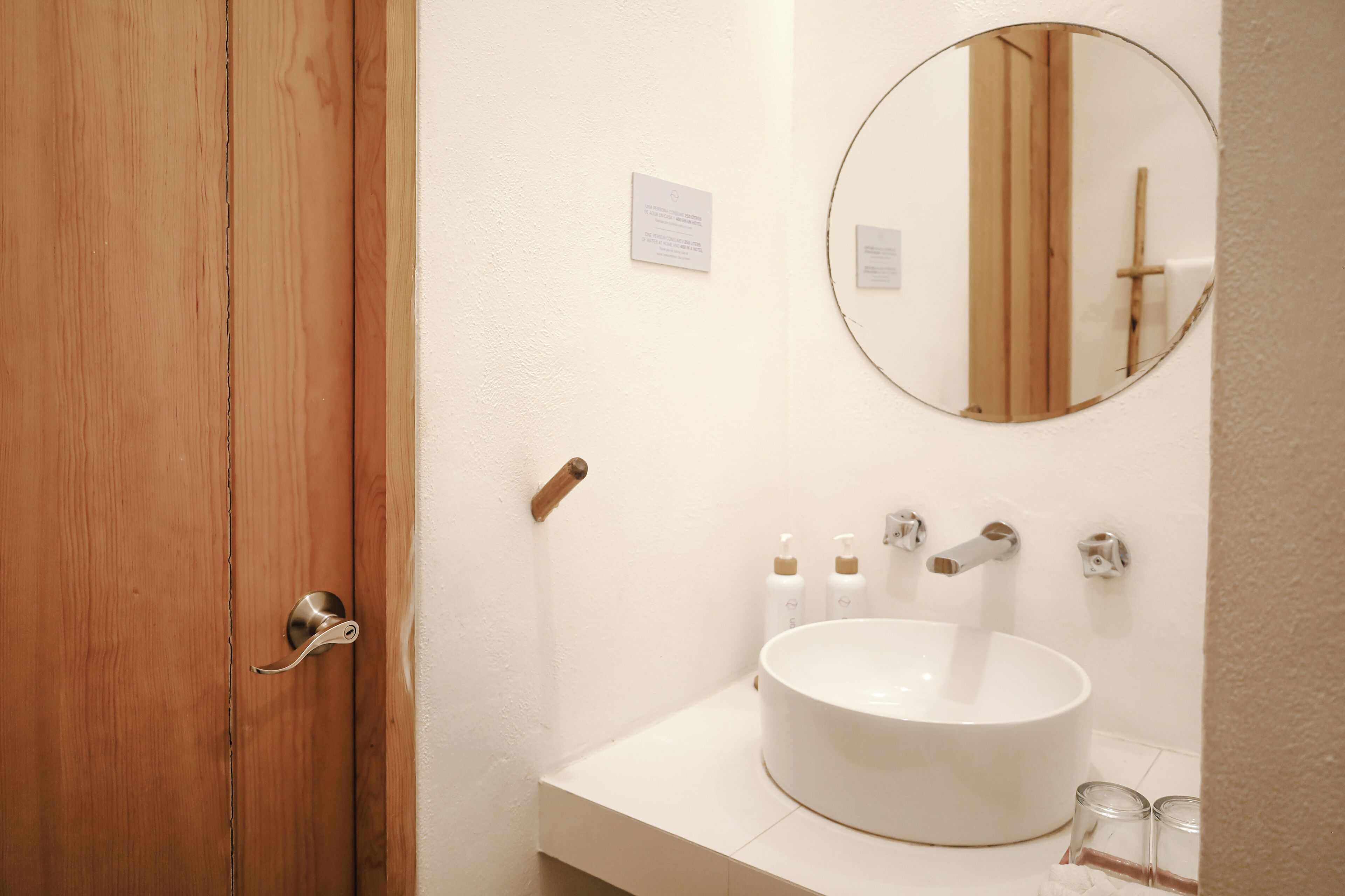 Un baño con puerta de madera, un lavabo blanco, un espejo redondo y un perchero para toallas.