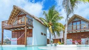 A resort with two thatched-roof bungalows, a pool, and a palm tree. - Punta Blanca | Beachfront Boutique Hotel (Costa Mujeres)