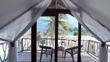 A covered outdoor seating area with a view of a beach and palm trees.