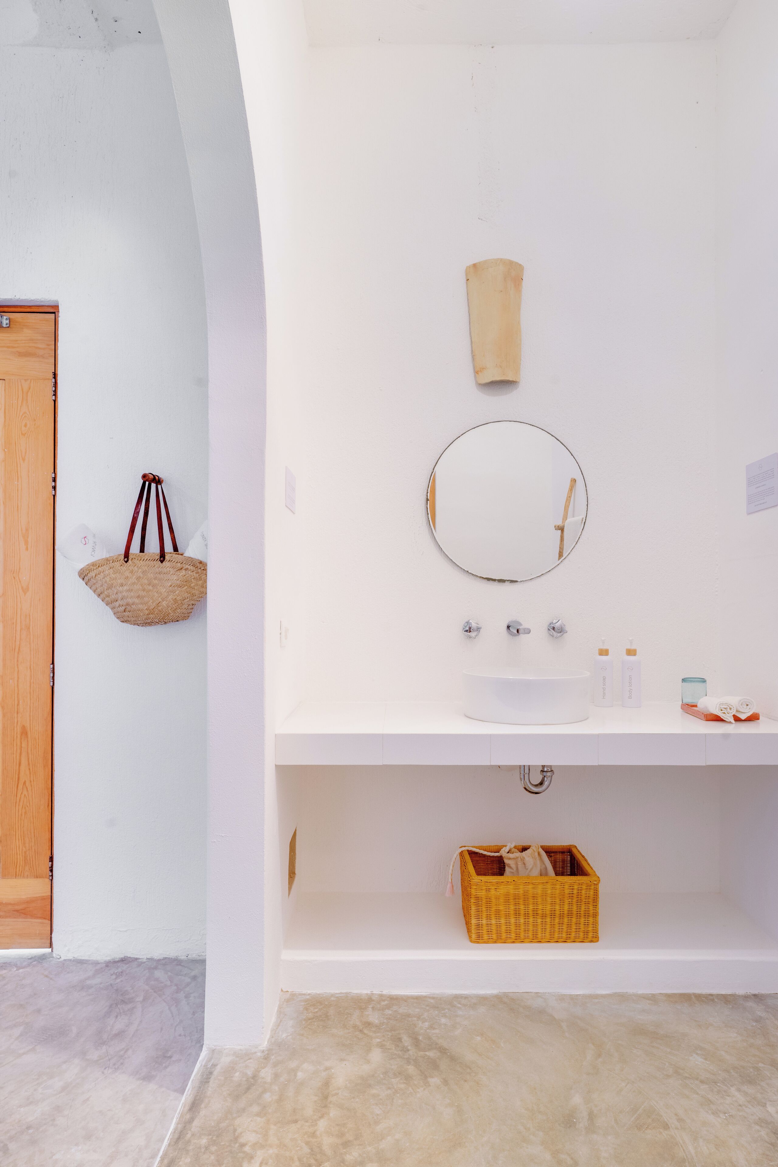 A bathroom with a white sink, a round mirror, and a wooden door.