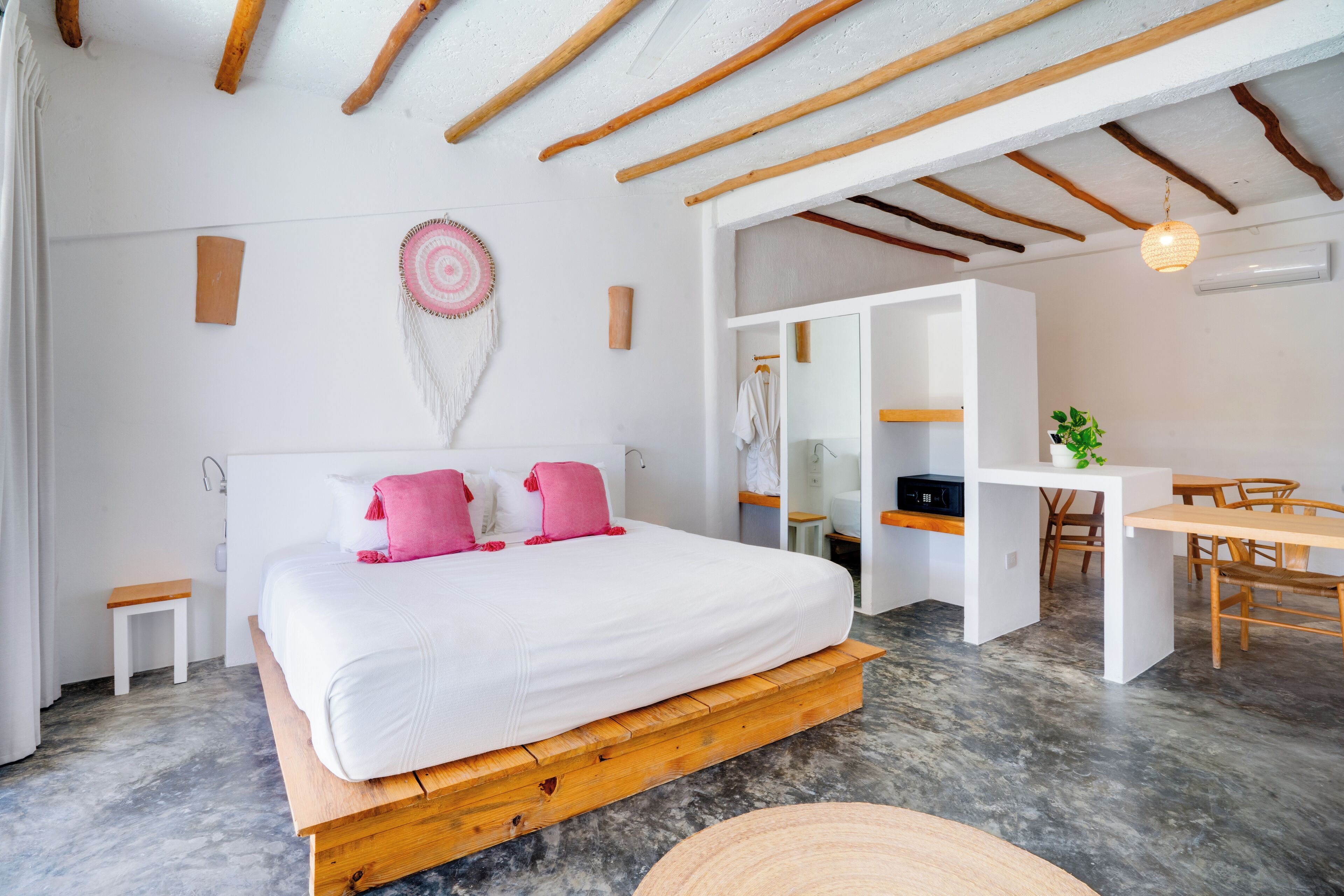 A modern bedroom with a wooden platform bed, a small bedside table, a wall-mounted decorative item, and a dining area with a table and chairs.