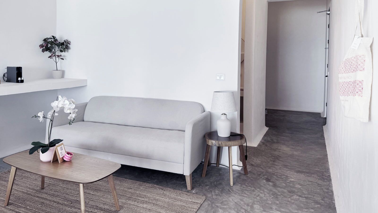 Ett modernt vardagsrum med en grå soffa, ett litet runt bord, en orkidé i en kruka och en lampa på ett sidobord.