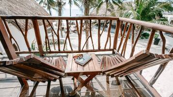 Un banco de madera con una mesita de vidrio, un libro y gafas de sol encima, situado en una terraza con vistas a palmeras y la playa.