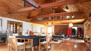 Une pièce spacieuse avec un haut plafond en bois, un coin repas comprenant une table et des chaises, et un mur en briques en arrière-plan.