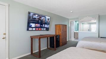 A hotel room with a television mounted on the wall displaying a movie, a wooden cabinet, a small table, and two beds.