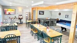 A dining area with wooden tables and chairs, a pool table, and a television mounted on the wall. - The Bradford (Branson)