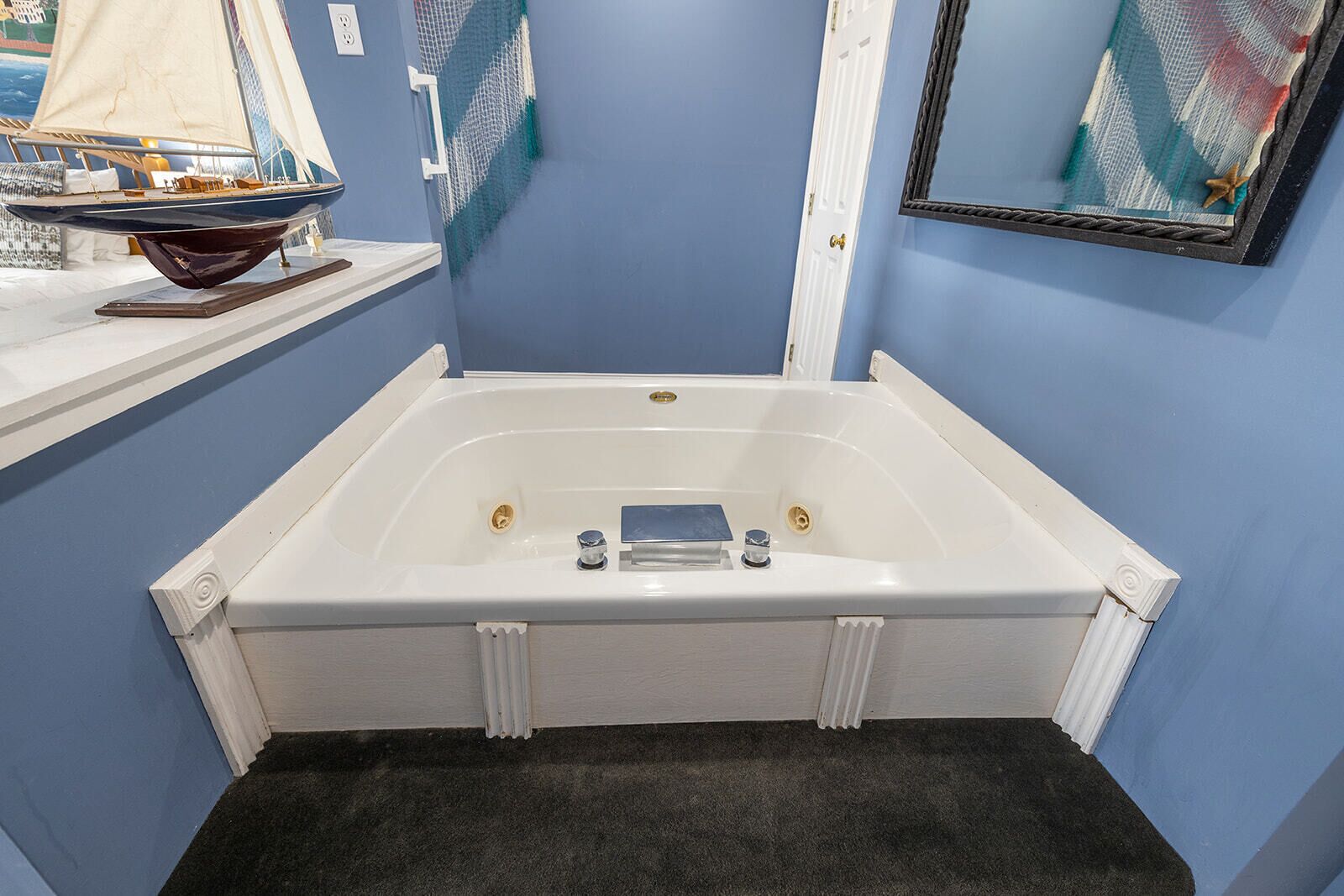 A bathroom with a white bathtub, a small shelf with a decorative item, and a framed artwork on the wall.