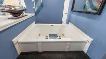 A bathroom with a white bathtub, a small shelf with a decorative item, and a framed artwork on the wall.