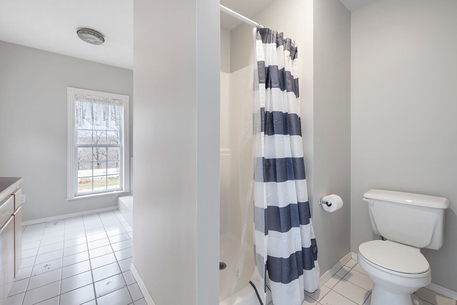 A bathroom with a white toilet, a shower curtain, and a window with a view of trees.