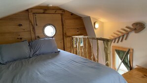 A bedroom with a bed, a wooden ceiling, a window, and a wooden staircase. - Adorable Tiny House in Picturesque Seaside Village (Warren)