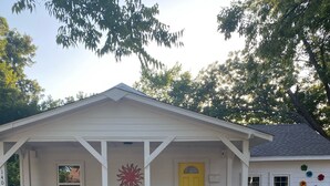 Une maison blanche avec un porche, une porte jaune et une clôture en bois peinte en blanc.
