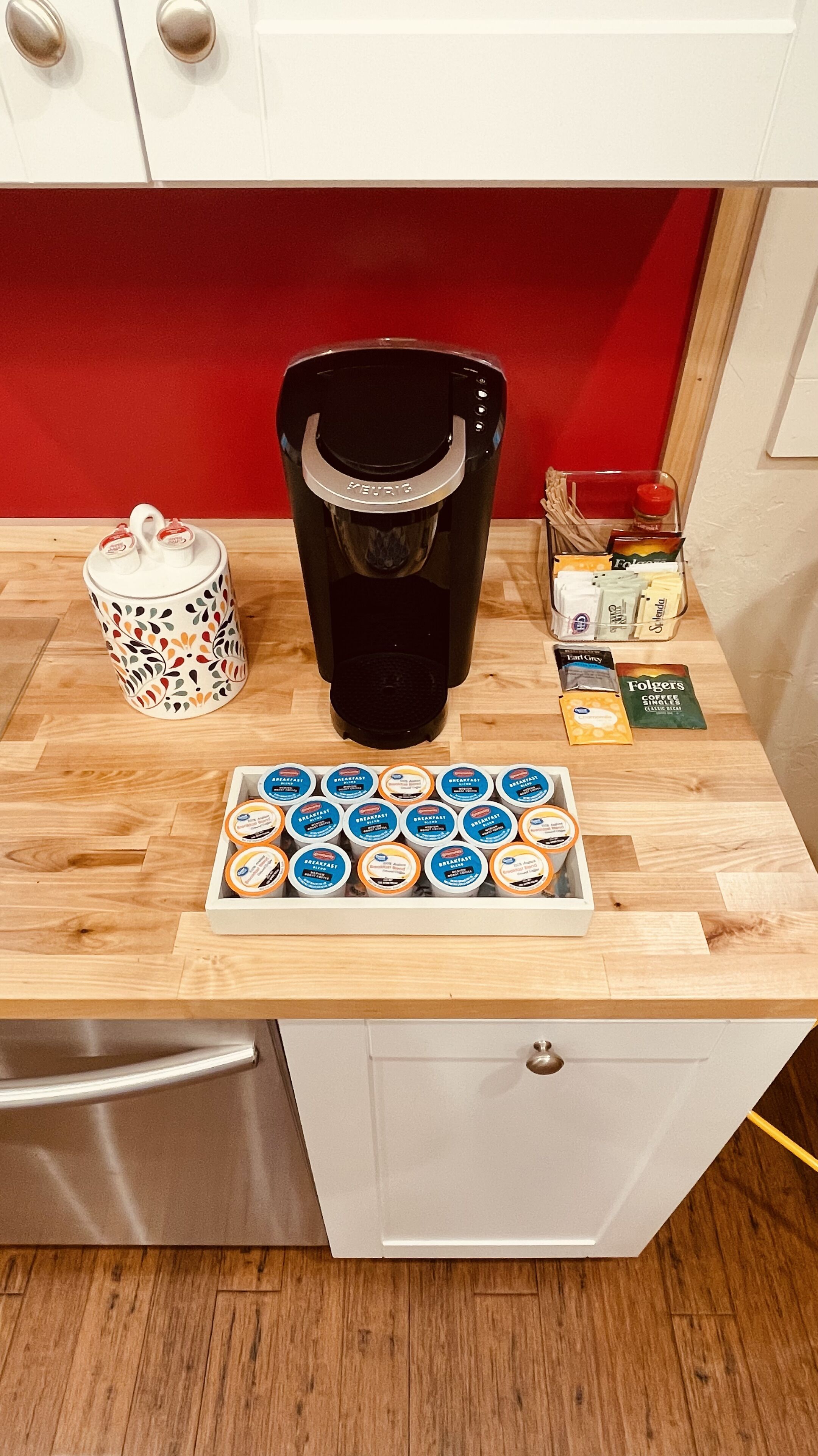 Een keukenblad met een koffiezetapparaat, een mok, een bak koffiekapsules en een doos Folgers coffee singles.